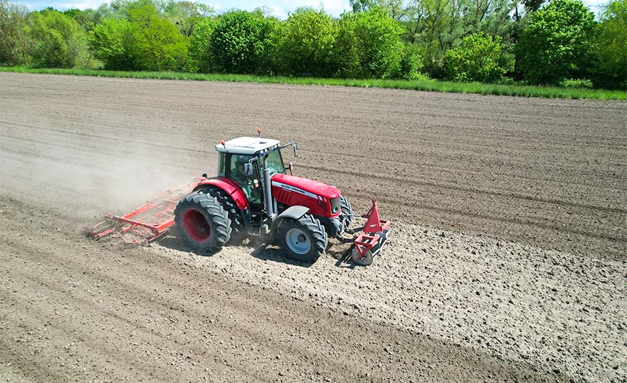Ein roter Traktor, der mit einem automatischen Lenksystem ein Ackerfeld bearbeitet, veranschaulicht die moderne Präzisionslandwirtschaft.